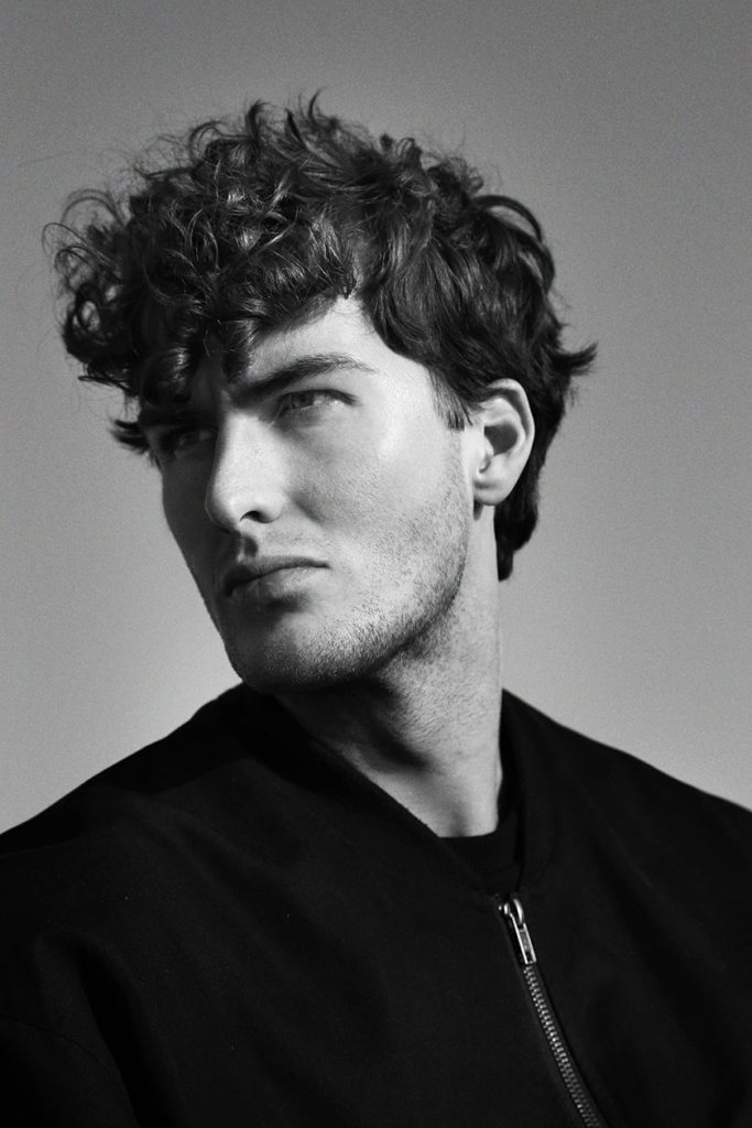 Black-and-white photo of male model with curly hair.