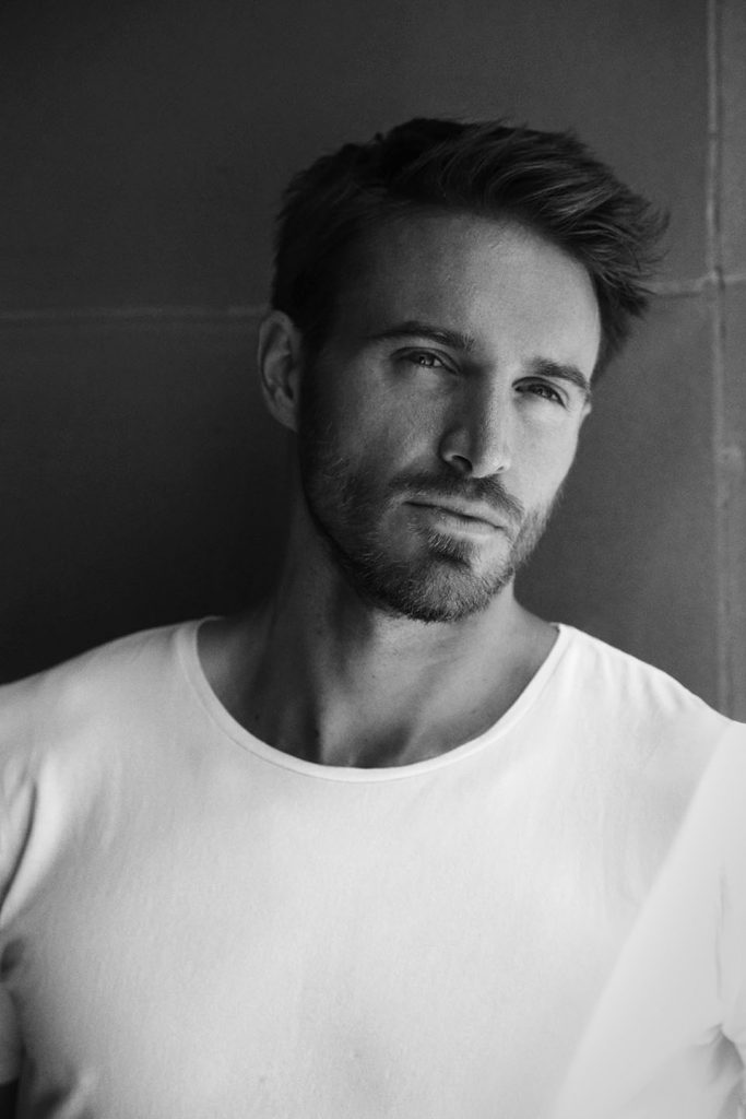 Black-and-white portrait of bearded male model in white T-shirt.