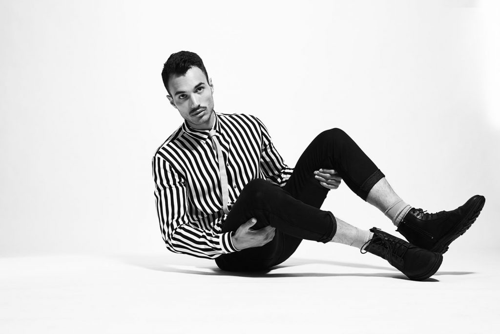 Black-and-white photo of male model in striped vintage shirt sitting on floor.